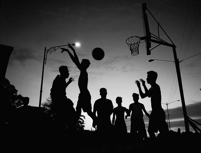 Silhouette people playing basketball against sky during sunset