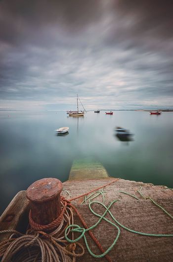 High angle view of rope tied on bollard by river at harbor against cloudy sky