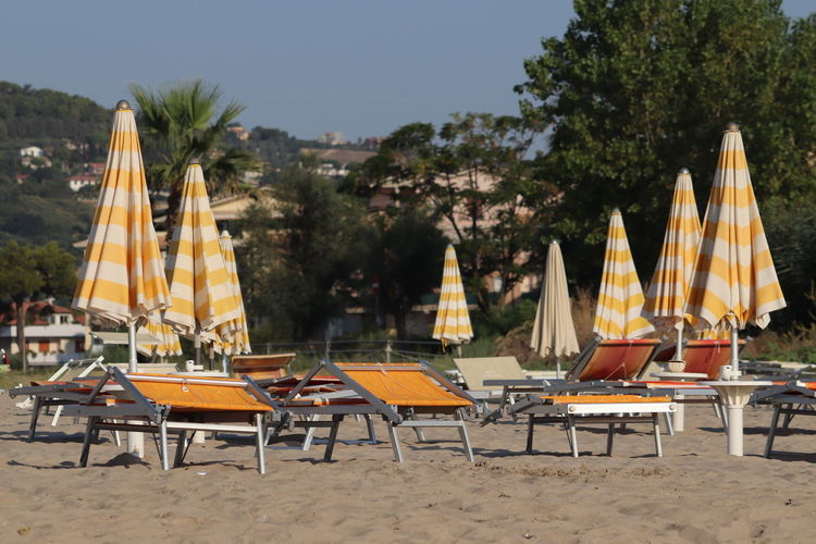 Chairs and tables on beach against trees