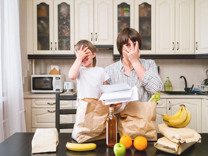 Father and son covering face with hand in kitchen
