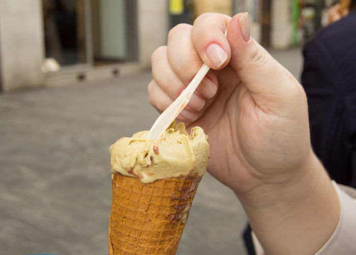 Pistachio ice cream in a waffle cone with a spoon close-up in women's hands.