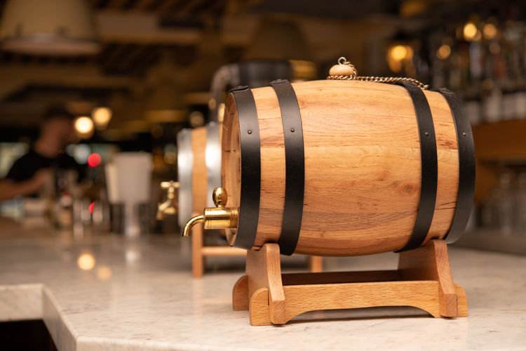 Close up of little wooden barrel and faucet on bar counter, out of focus people in background