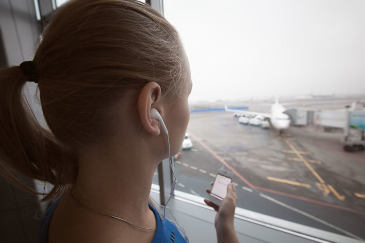 Close-up of young woman listening music on smart phone while standing by window
