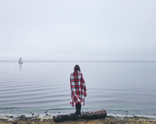 Rear view of woman standing at sea shore during foggy weather