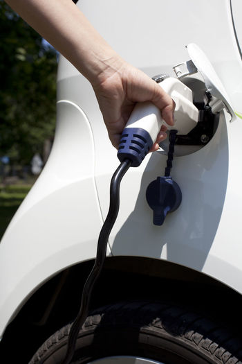 Cropped hand of person charging white electric car