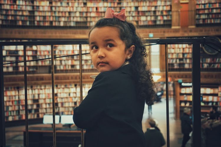 Cute girl looking away while standing by railing in library