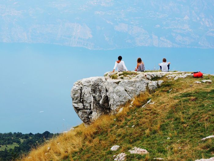 Rear view of people sitting on mountain against lake