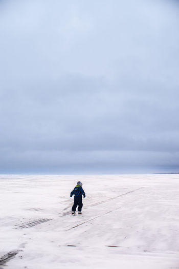 Rear view of person ice-skating on frozen lake peipus against sky