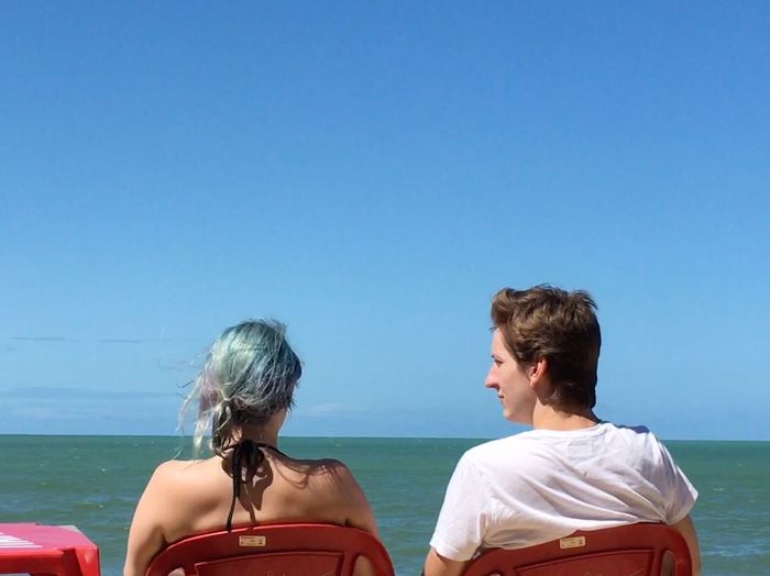 Rear view of couple sitting on sea against clear blue sky