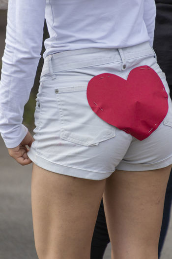 Midsection of young woman with heart shape paper on shorts