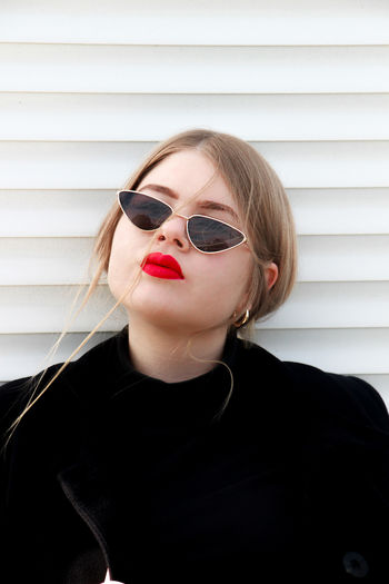 Portrait of young woman wearing sunglasses against wall