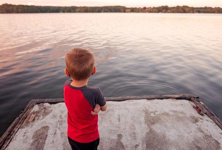 Rear view of boy looking at lake during sunset
