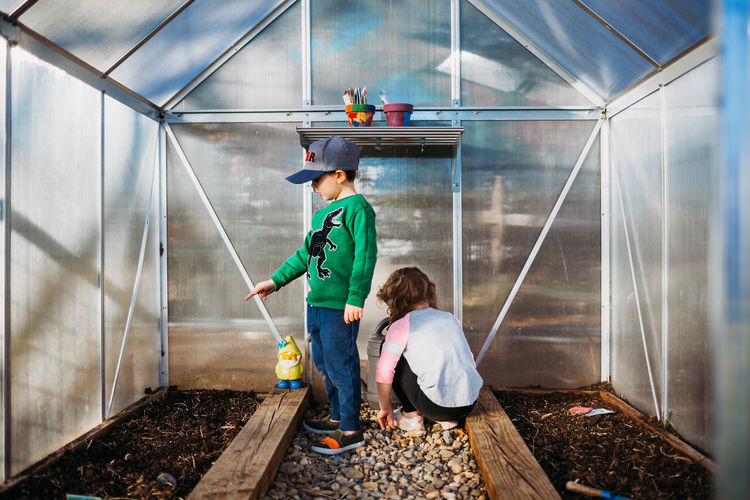 Young brother pointing at dirt in greenhouse with sister in spring
