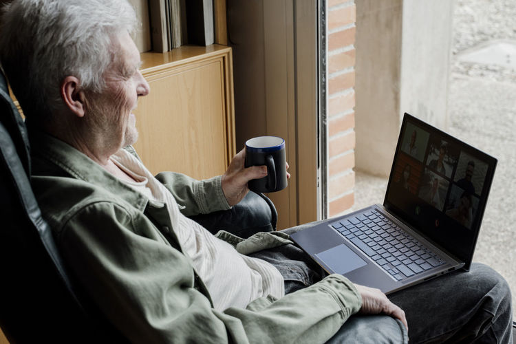 Senior man with laptop holding coffee mug at home