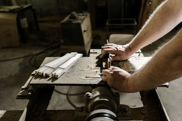 Side view of unrecognizable crop craftsman working in dirty workshop at dusty workbench while standing with wooden folding fan