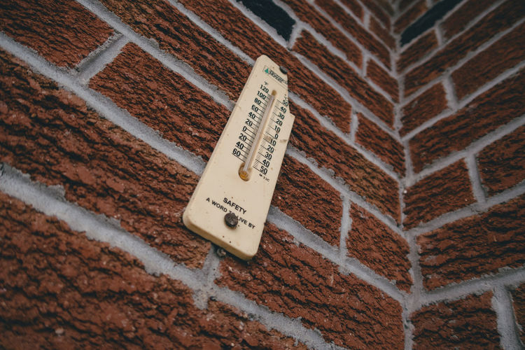 Looking up at thermometer on brick wall.