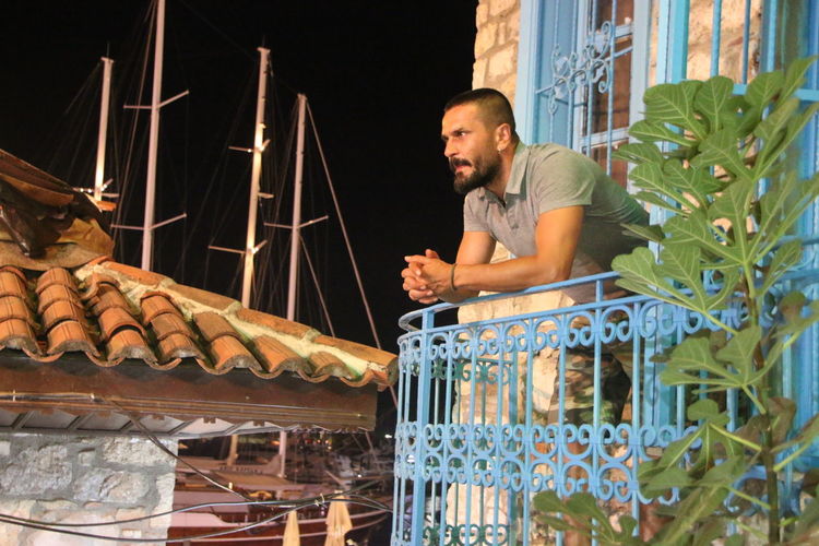 Thoughtful man standing in balcony against harbor at night