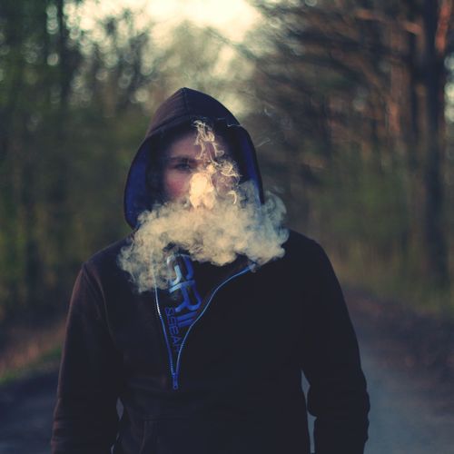 Portrait of man exhaling smoke against trees