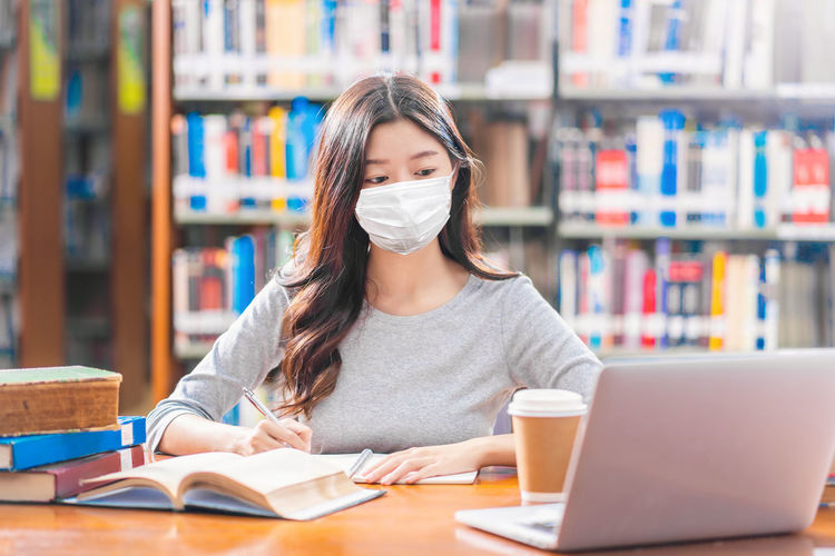Young woman wearing mask studying in library