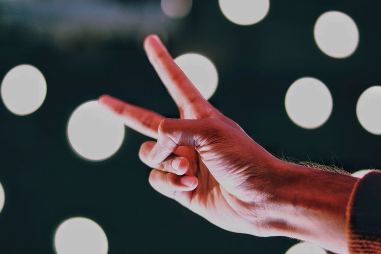 Cropped hand of man gesturing peace sign at night