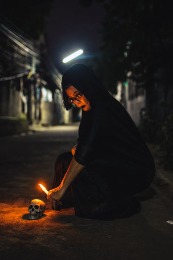 Side view of woman holding lit candle at night
