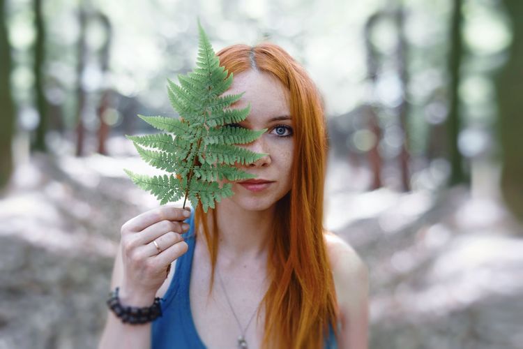 Portrait of redhead young woman holding leaves in forest