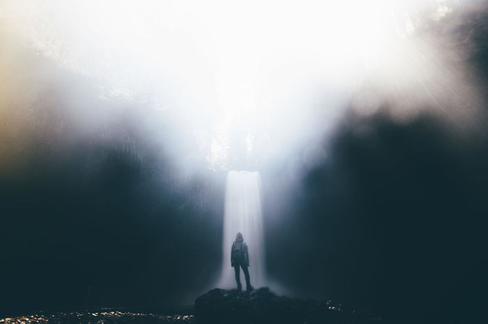 Rear view of woman standing by waterfall in foggy weather