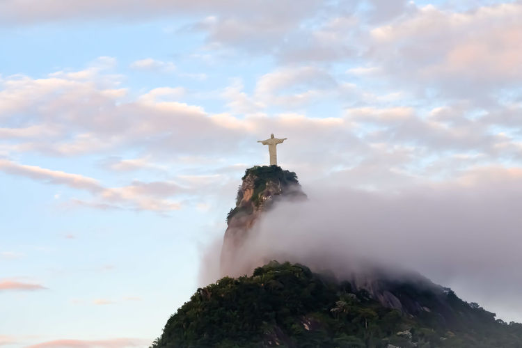 Low angle view of jesus christ statue on mountain against cloudy sky