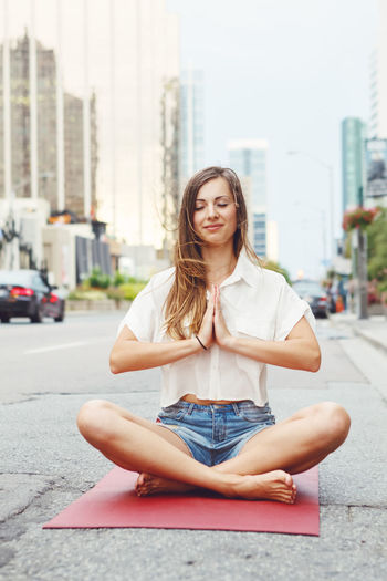 Smiling woman mediating while sitting on road in city