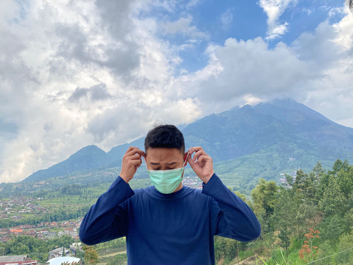 Young man wearing mask standing against mountain and sky