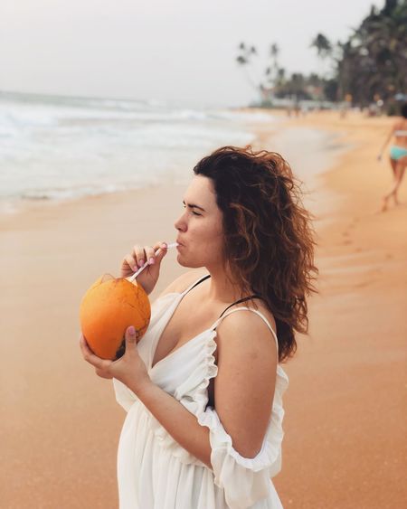 Woman drinking coconut water while standing at beach