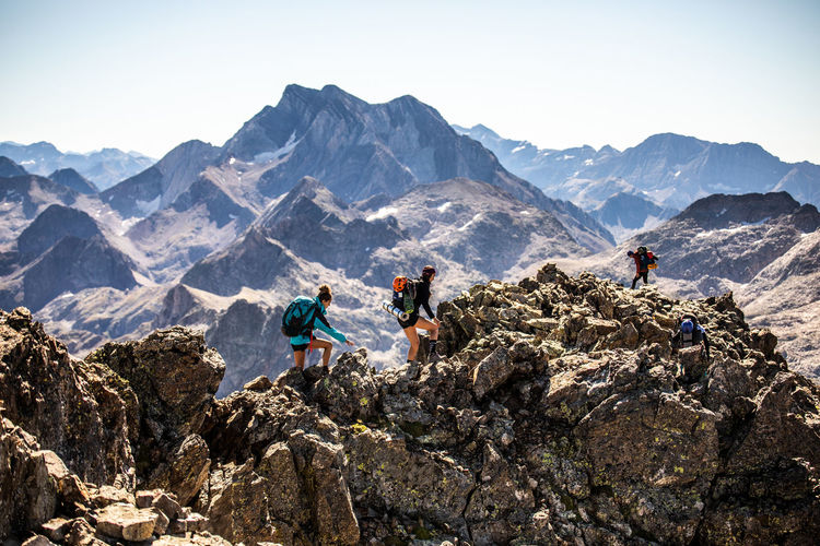 Group of mountaineers with backpacks climbing rough rocky mountain peak during summer adventure in pyrenees