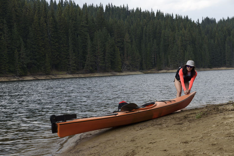 Woman bending by kayak at lakeshore