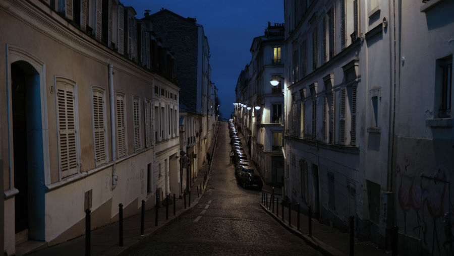 Narrow street amidst buildings in city at dusk