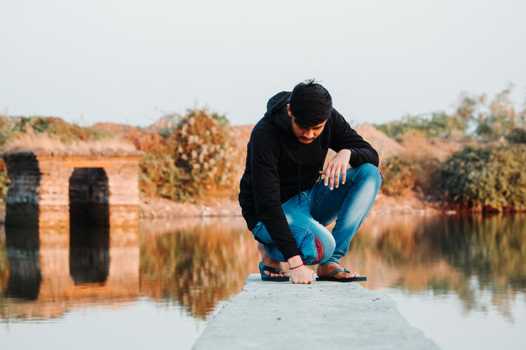 Man kneeling on concrete over lake against clear sky