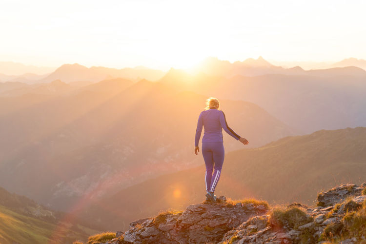 Rear view of woman standing on mountain peak against sky during sunrise