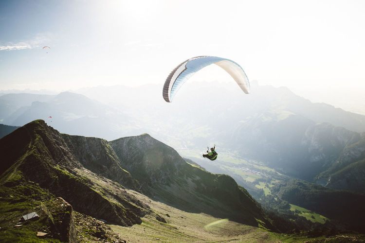 Man paragliding over mountains against sky