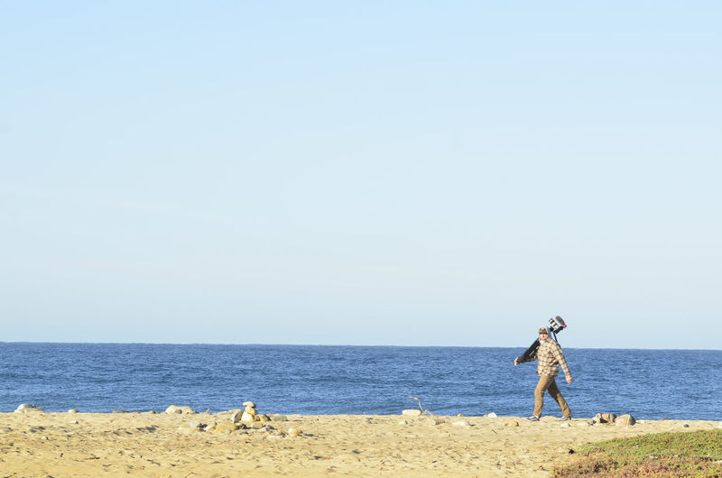 Young man carries video camera on tripod  walking on ocean beach in baja california sur, mexico
