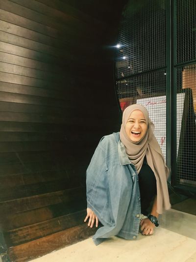 Portrait of cheerful woman wearing hijab crouching on floor