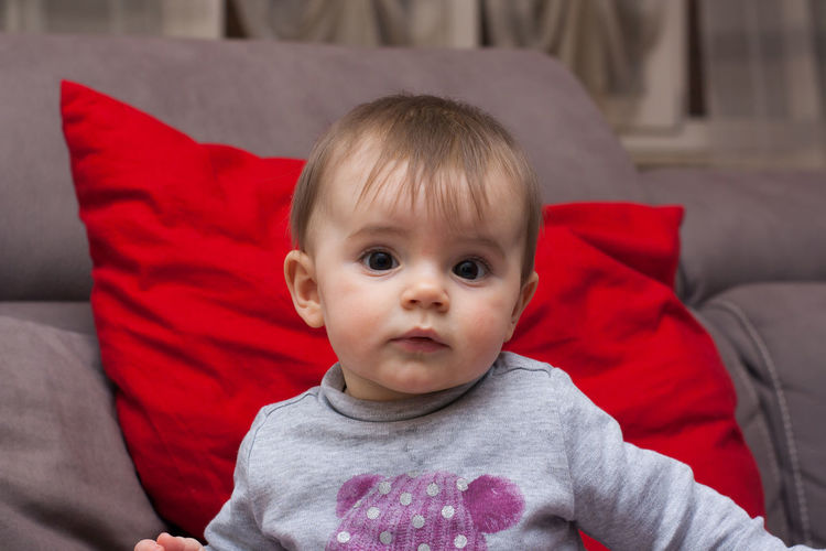 Portrait of cute baby girl against sofa at home
