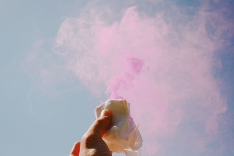 Cropped hand of person holding tissue amidst smoke against sky