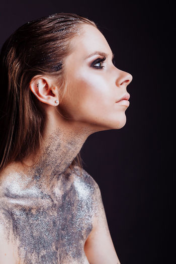 Close-up of shirtless woman with glitter against black background