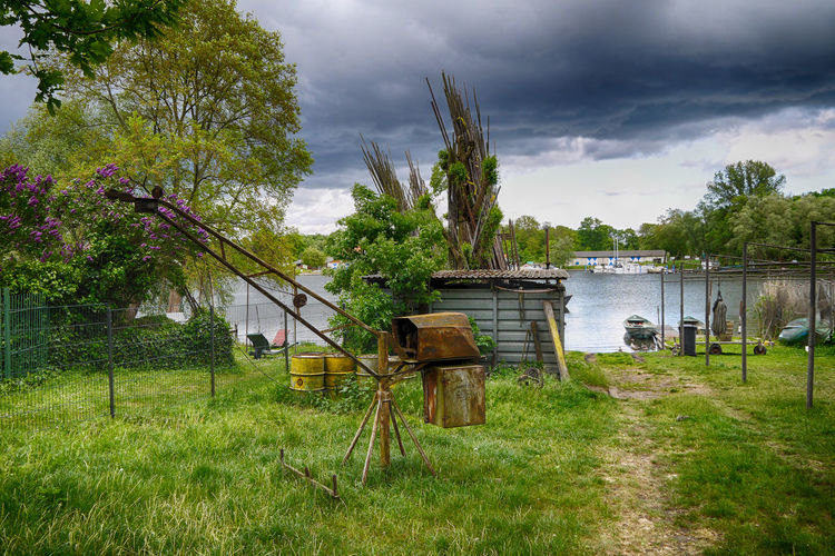 Equipment on grassy field by river against cloudy sky
