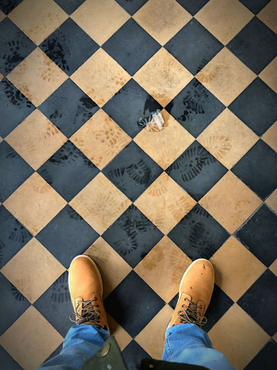 Low section body of a man with blue jeans and winter boots on a tiled checkerboard pattern floor