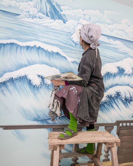 Mature woman artist paints a mural on a marine theme on the wall