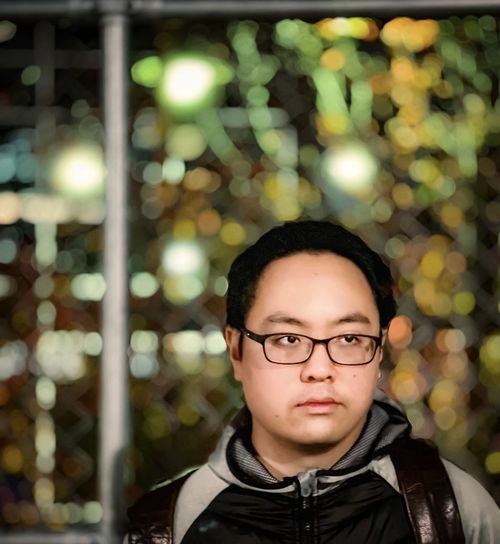 Portrait of young man wearing eyeglasses against street and neon lights at night.