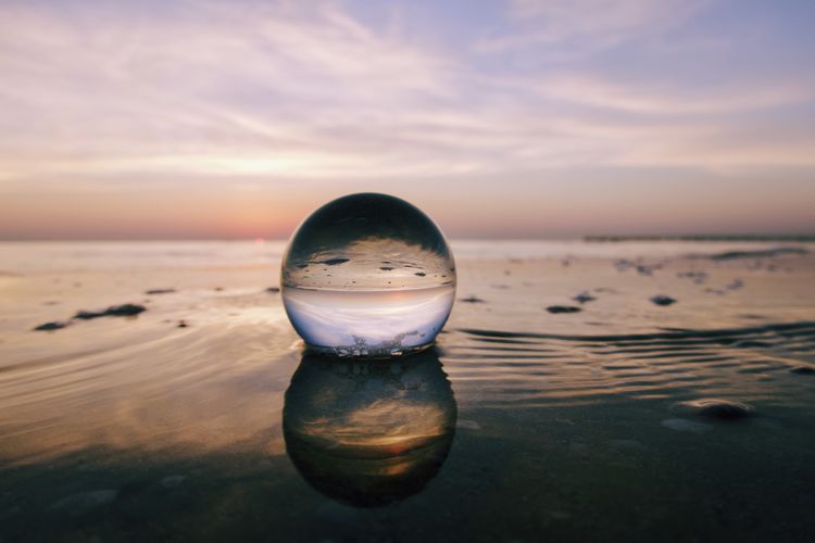 Close-up of crystal ball on beach against sky during sunrise 