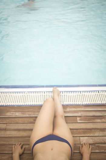 Low section of woman relaxing against swimming pool