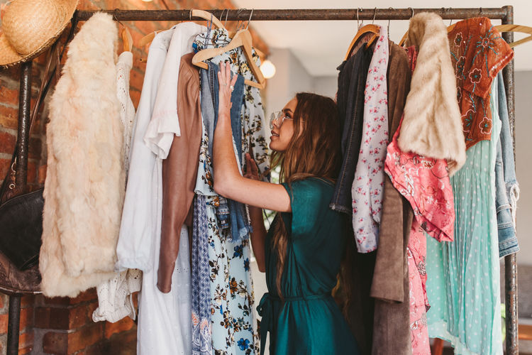 Side view of young woman hanging clothes on rack at home