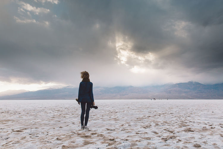 Rear view of woman standing on field against cloudy sky at death valley national park